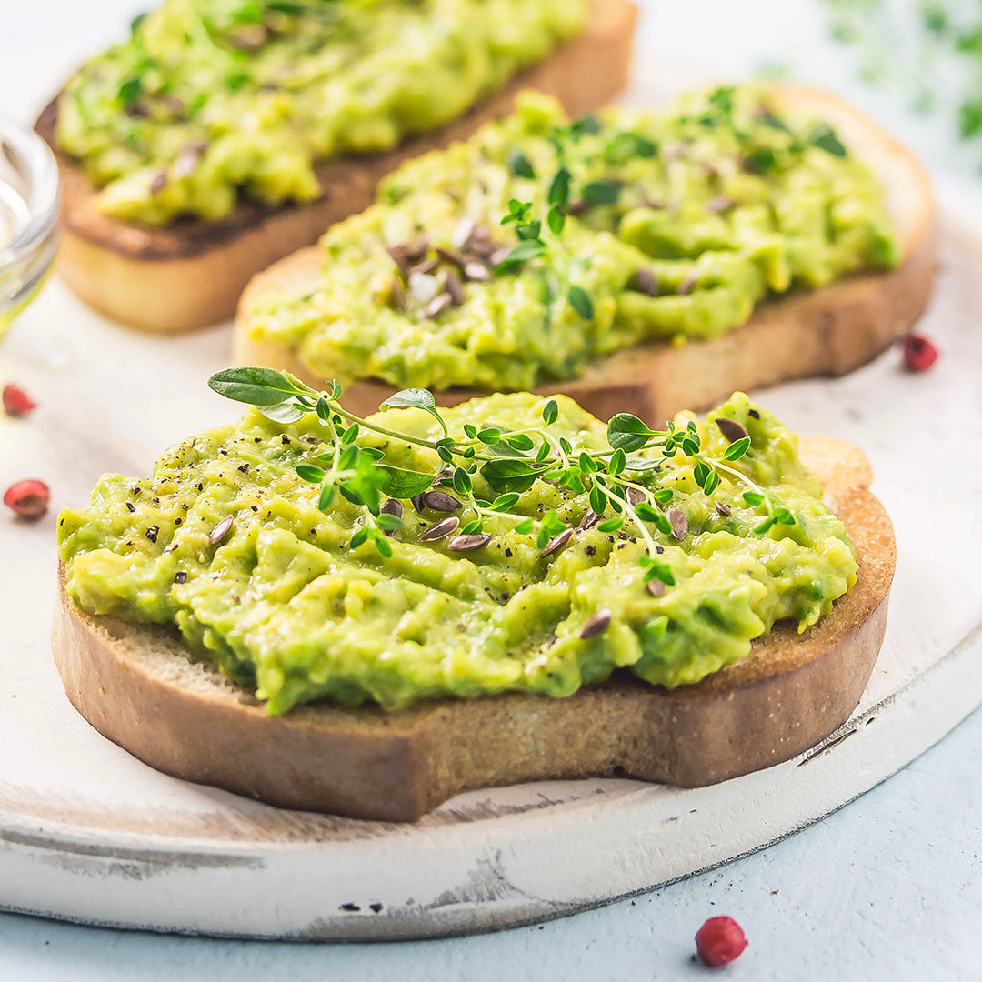 Mashed avocado in bread and silver platter, topped with sprouts and seeds