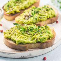 Mashed avocado in bread and silver platter, topped with sprouts and seeds