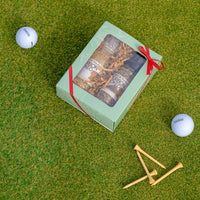 Gift set with a red ribbon on grass, surrounded by golf balls and tees.