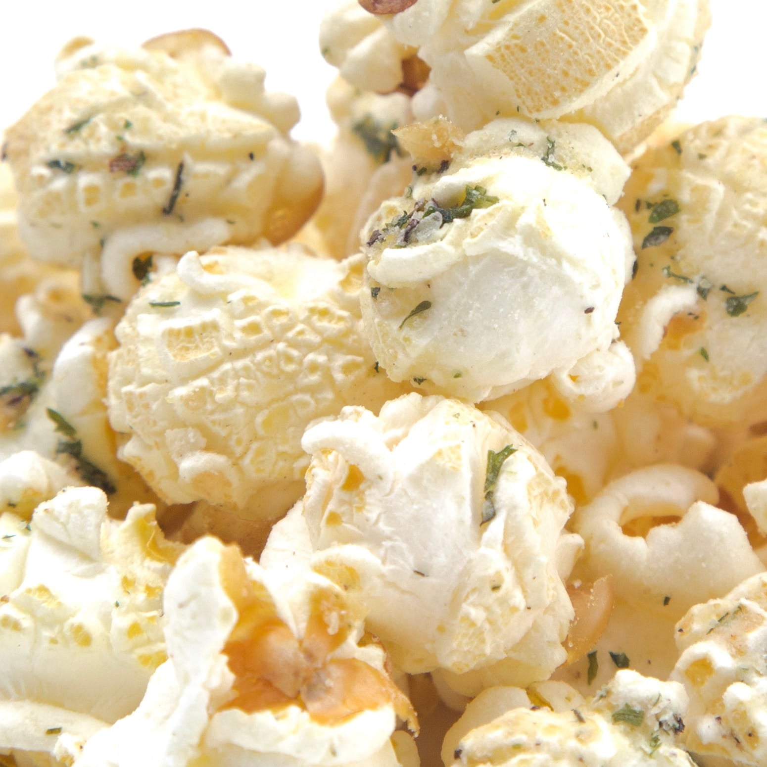 Close-up of fluffy popcorn mixed with herbs and melted butter, filling the frame against a white background.