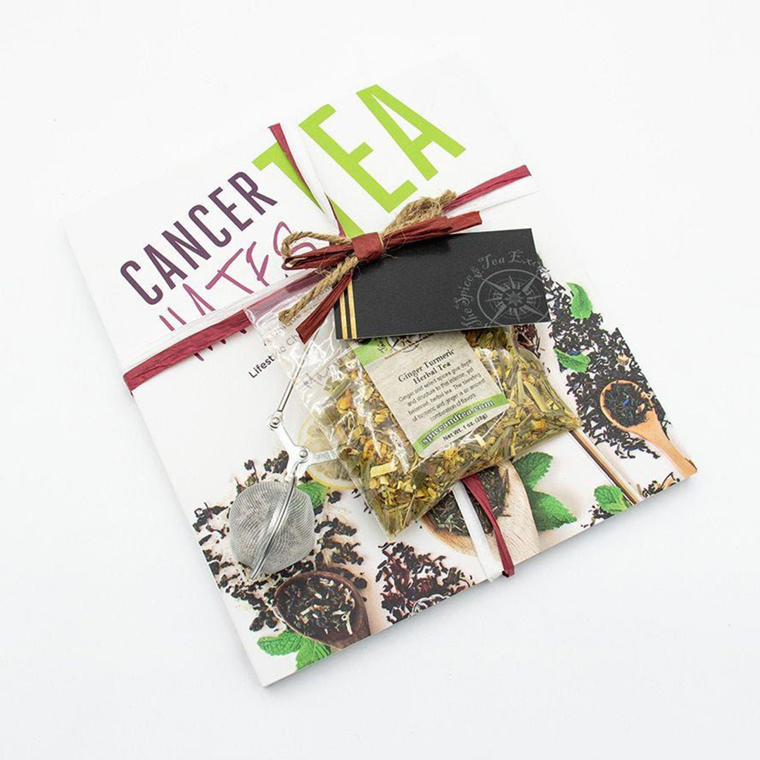 A flat-lay of the Cancer Hates Tea Book & Bundle - Ginger Turmeric, featuring the book, Ginger Turmeric Herbal Tea, a tea infuser, and a black gift tag tied with red ribbon—an ideal gift for tea and wellness fans.