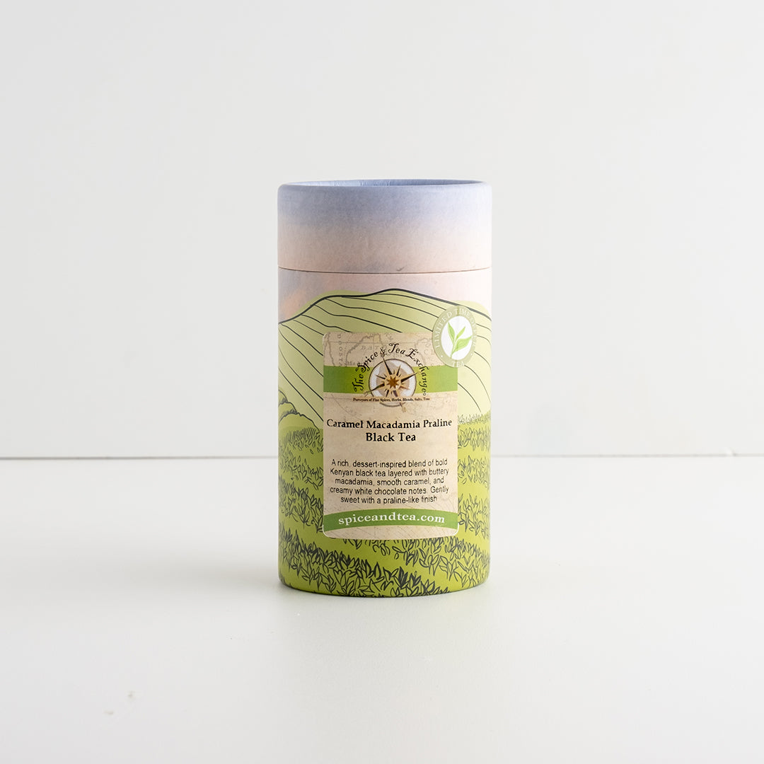 A cylindrical cardboard tube package for Caramel Macadamia Praline Black Tea, featuring a scenic green hill illustration on a white background.