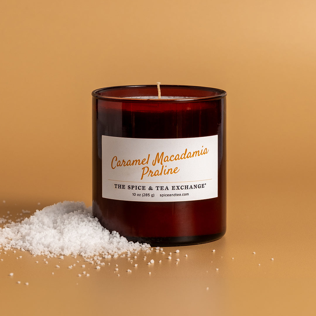 Caramel Macadamia Praline Candle on amber background in amber glass jar next to snow pile