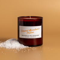 Caramel Macadamia Praline Candle on amber background in amber glass jar next to snow pile
