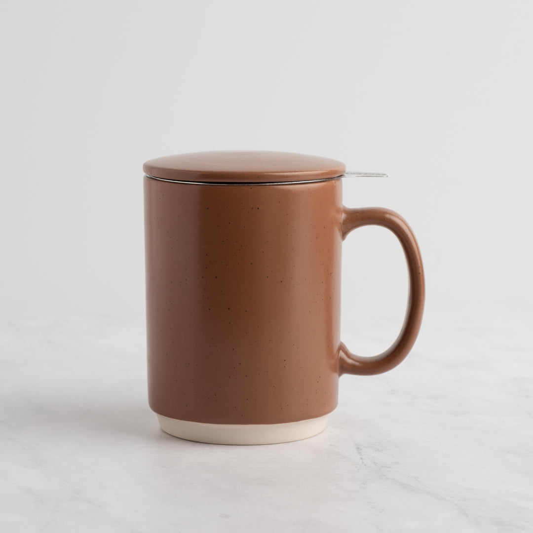 A speckled Mocha Mousse ceramic mug with a matching lid and a small metal spoon resting on the rim, set against a clean white background.