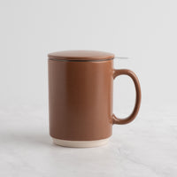 A speckled Mocha Mousse ceramic mug with a matching lid and a small metal spoon resting on the rim, set against a clean white background.