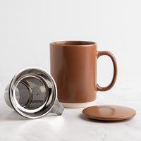 A mocha mousse ceramic mug with a matching lid and stainless steel tea infuser, displayed on a light marble surface against a white background.