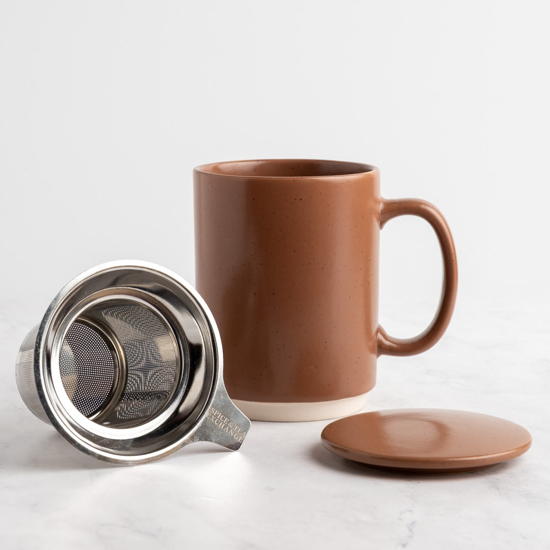 A mocha mousse ceramic mug with a matching lid and stainless steel tea infuser, displayed on a light marble surface against a white background.
