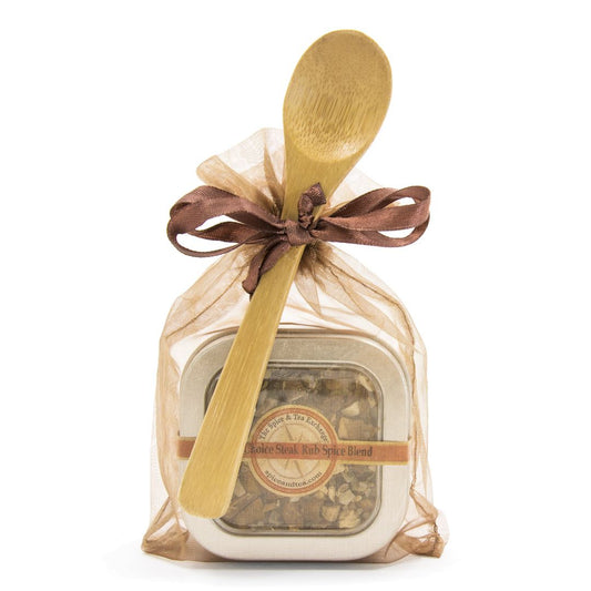 The Chef's Choice Spice Blend - Spice Tin with Spoon comes in a sheer beige gift bag tied with a brown ribbon, with a wooden spoon placed on top.