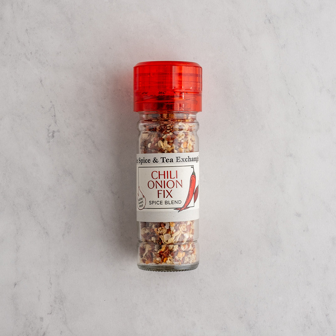 A bottle of Chili Onion Fix Spice Blend by Spice & Tea Exchange, featuring a red shaker cap and a white label, set against a light gray marble background.