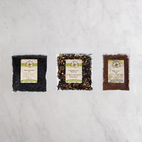 Three clear plastic bags of chocolate tea and a sugar arranged side by side on a white marble surface.