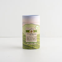 A cylindrical cardboard tube package of Chocolate Candy Cane Black Tea, featuring a pastel landscape label with green hills and a blue sky gradient, set against a plain white background.