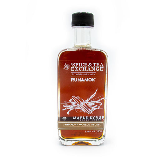 A clear glass bottle labeled Spice & Tea Exchange x Runamok holds Organic Cinnamon Vanilla Maple Syrup, featuring drawings of cinnamon sticks and vanilla pods that highlight its unique flavor.