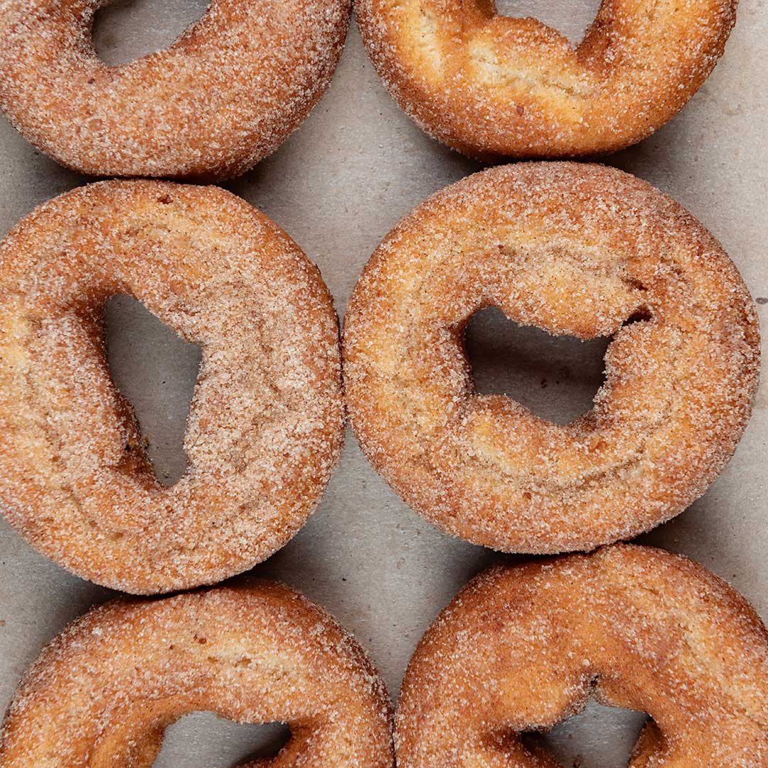 Six sugar-dusted cinnamon donuts arranged in two columns on a neutral gray surface.