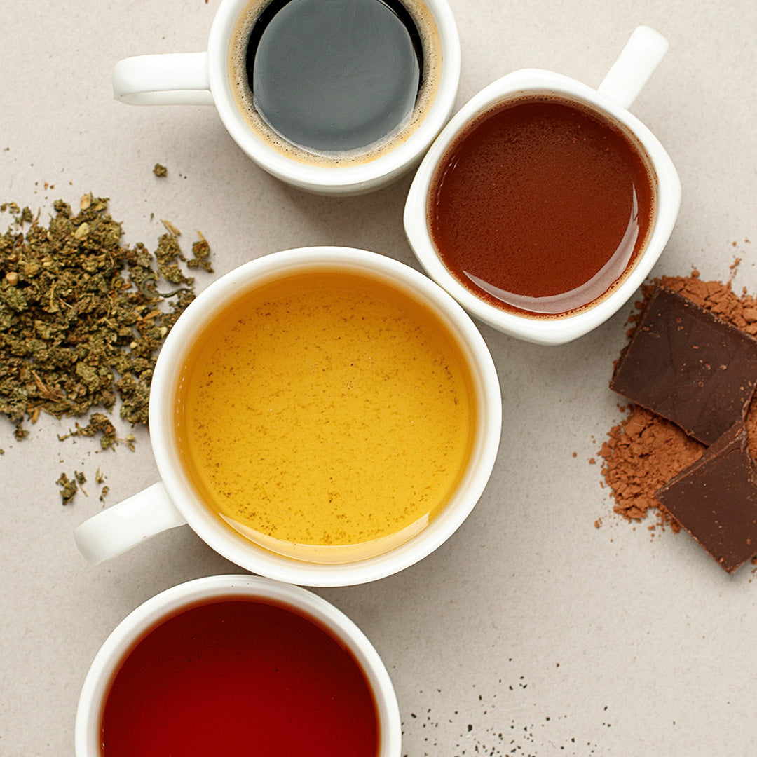 Four white ceramic cups filled with different colored beverages