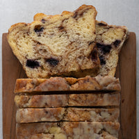 Sliced multicolored marble bread with dark cinnamon swirls, arranged on a wooden cutting board against a light gray background.