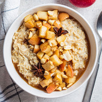 Bowl of oatmeal with apples and nuts on a light background