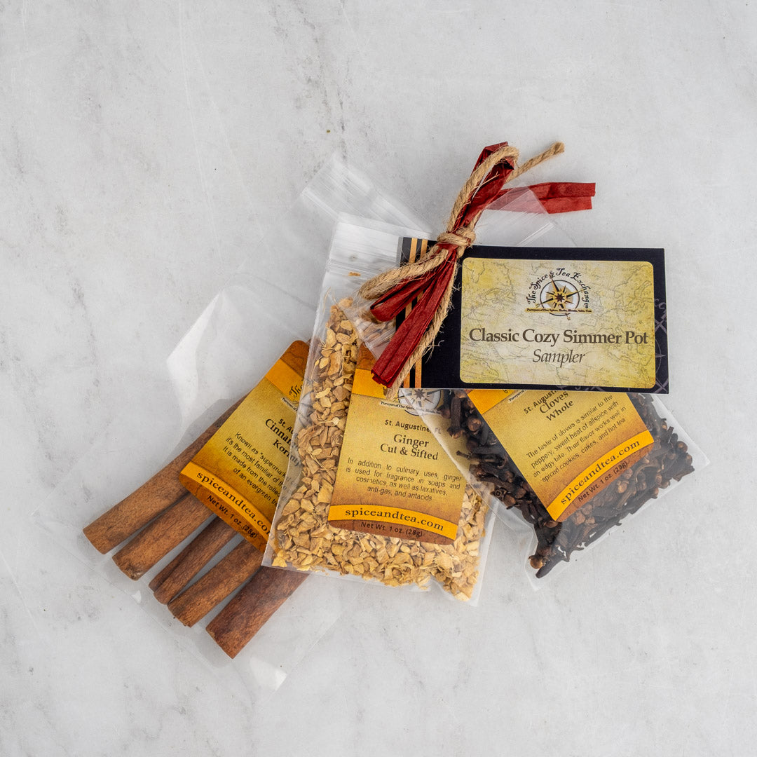 The Classic Cozy Simmer Pot Sampler includes clear bags of cinnamon sticks, cut ginger, and whole cloves tied with raffia and a tag—perfect for adding a cozy touch to your home.