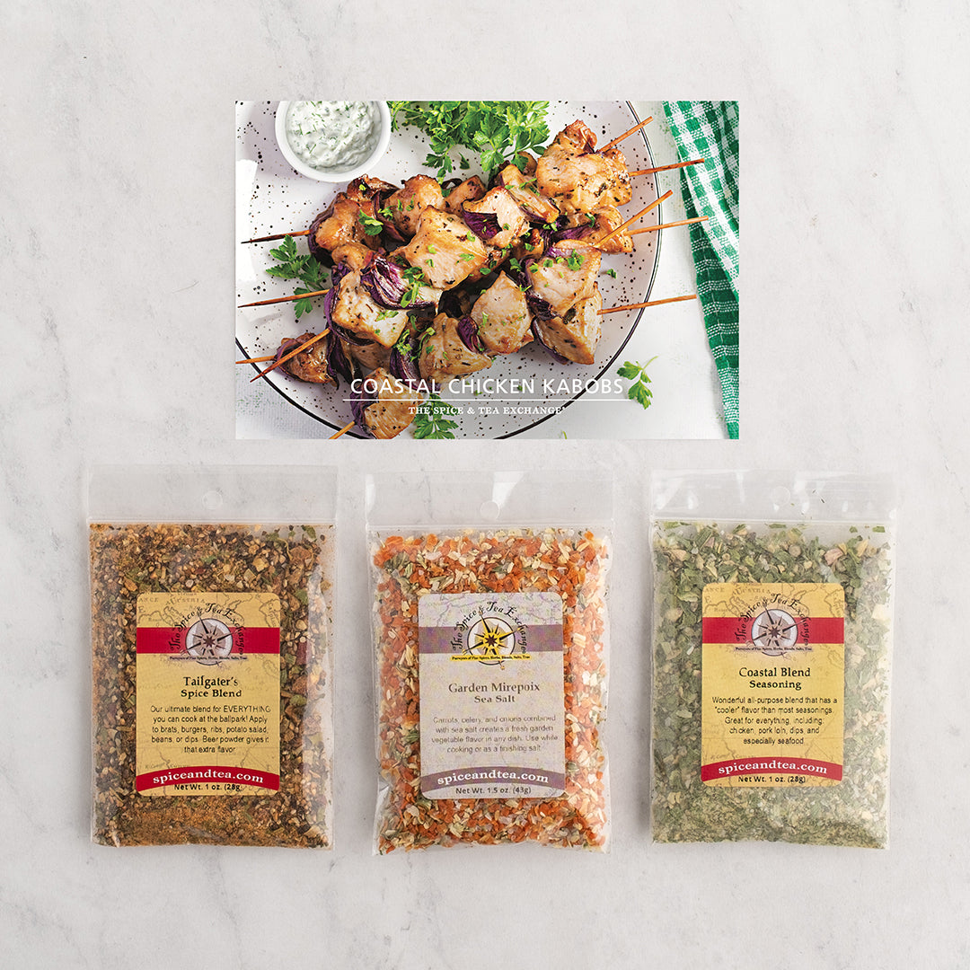 Three packaged seasoning blends are displayed on a white marble surface below a photo of grilled chicken kabobs with herbs and a side of dipping sauce.