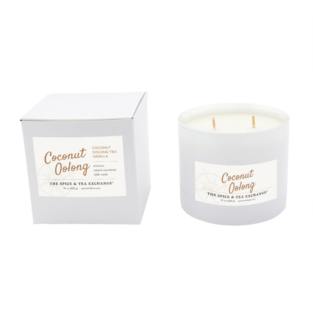A coconut oolong scented candle in a frosted white glass jar next to its white cardboard packaging box, both featuring a white label with gold text from The Spice & Tea Exchange.