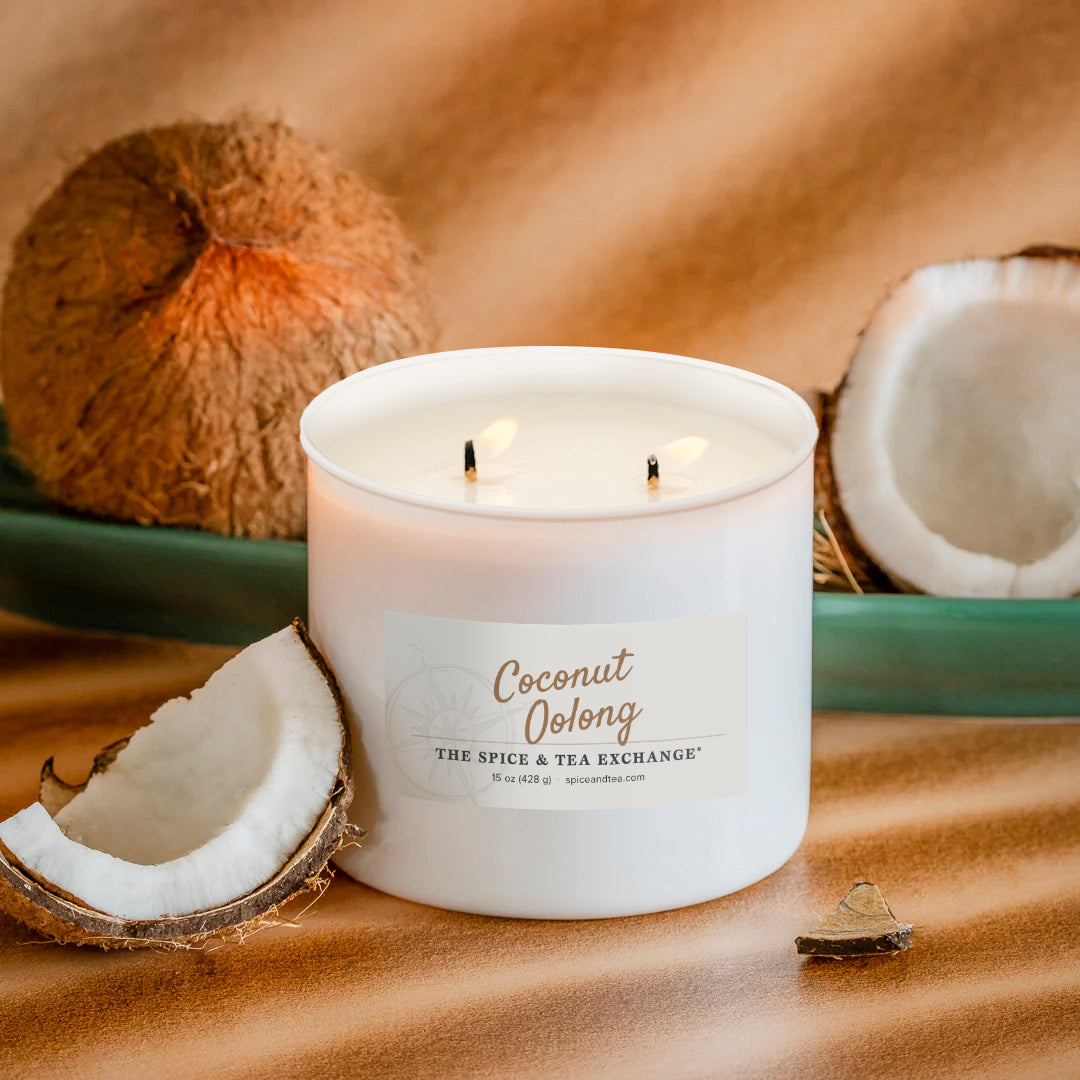 A white double-wick candle labeled 'Coconut Oolong' by The Spice & Tea Exchange, styled with whole and halved coconuts on a warm brown textured surface.