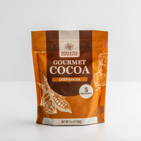 A stand-up pouch of Spice & Tea Exchange Gourmet Cocoa Cozy Cocoa, 3.4 oz (96g), on a light gray background.