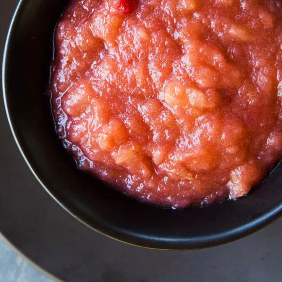 A close-up overhead shot of chunky red fruit sauce, likely apple or peach chutney, served in a black bowl.