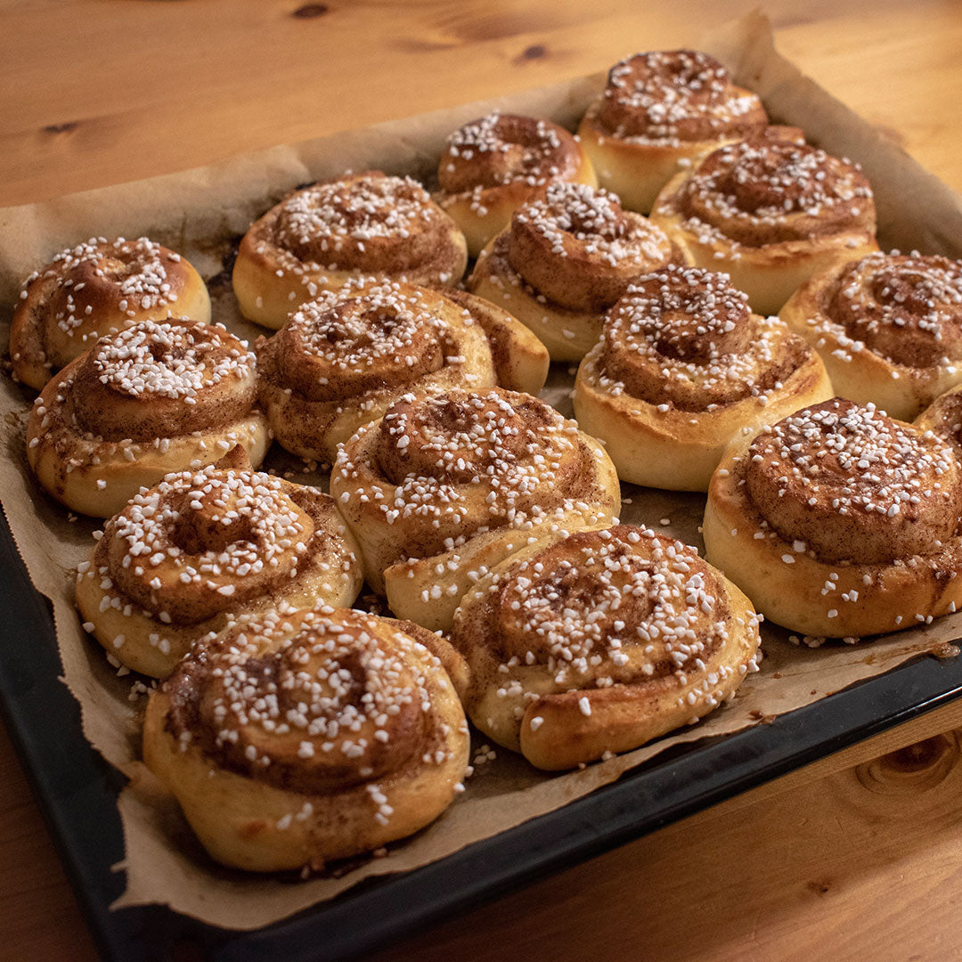 A tray of freshly baked cinnamon rolls topped with white sugar crystals, arranged on a parchment-lined baking sheet over a wooden table.