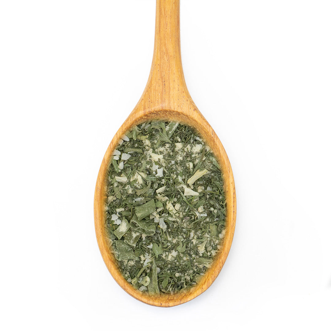 A wooden spoon filled with dried green herbs and small white pieces, photographed from above on a plain white background.