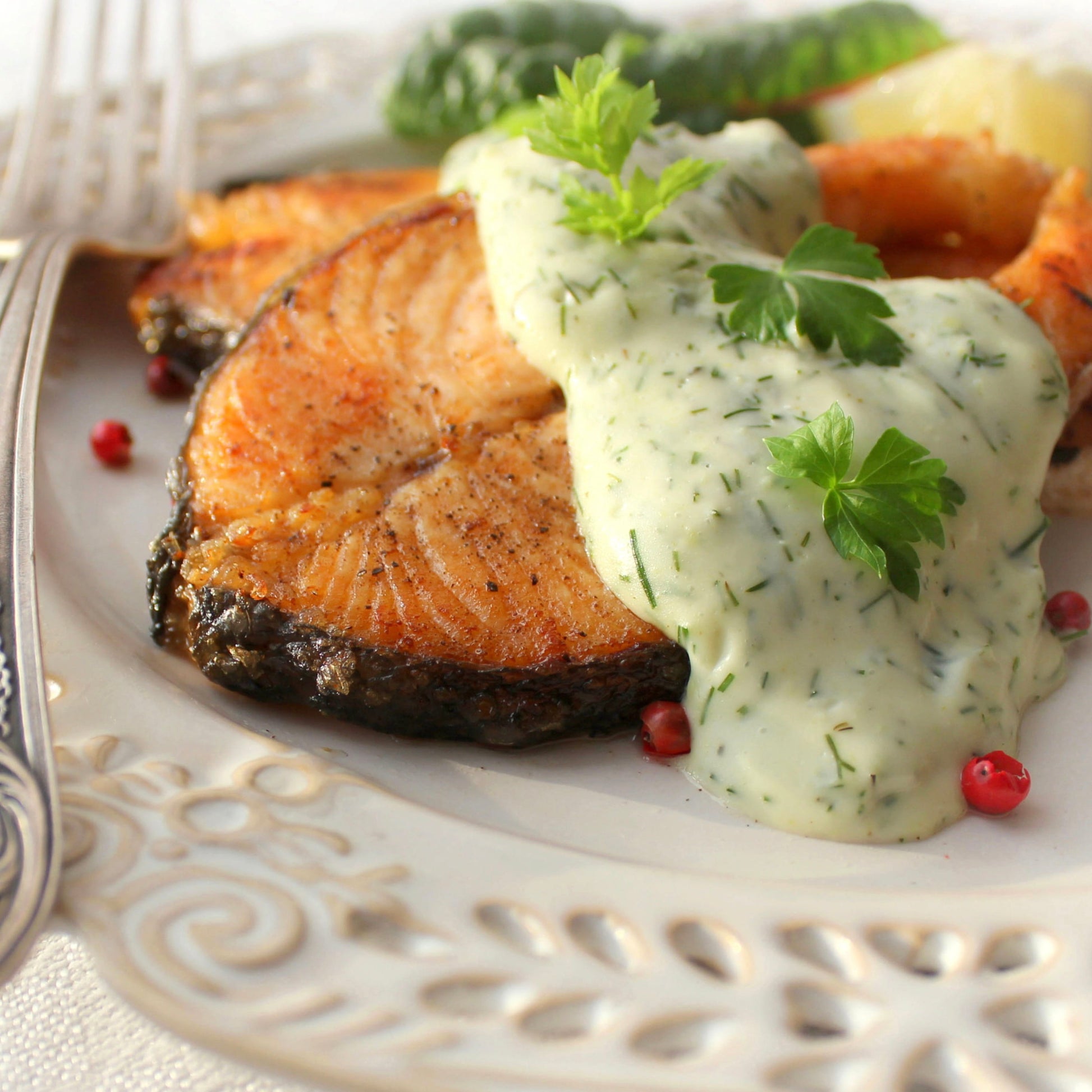 Pan-seared salmon fillets on a white plate with a creamy dill sauce, garnished with parsley, served with red pimento peppers and green beans.