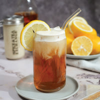 Glass of iced tea with lemon slices and whipped cream topping on a table.