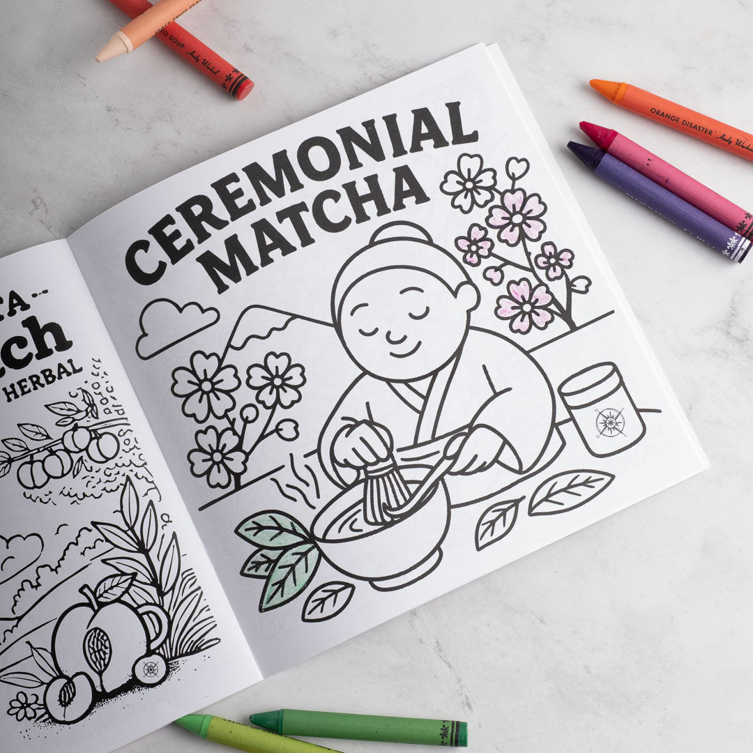 Coloring book open to a page with 'Ceremonial Matcha' text and illustrations, surrounded by crayons on a light surface.