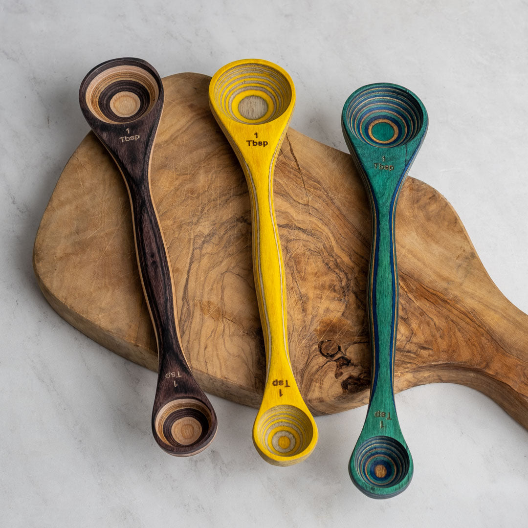 Lemon, peacock, and natural double-ended spoons with 1 tsp and 1 tbsp on each side. Sitting on wood board.