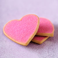 Three heart-shaped sugar cookies dusted with pink sugar, stacked on a soft lavender background.