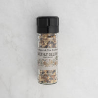 Earthly Delight Spice Blend comes in a clear jar with a black lid, showing its chunky herb and spice mix inside. The label displays herbs and spices on a white marble background. Ideal for adding bold flavor to meats, soups, and stews.