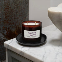 Candle in an amber glass jar with a label on a marble surface