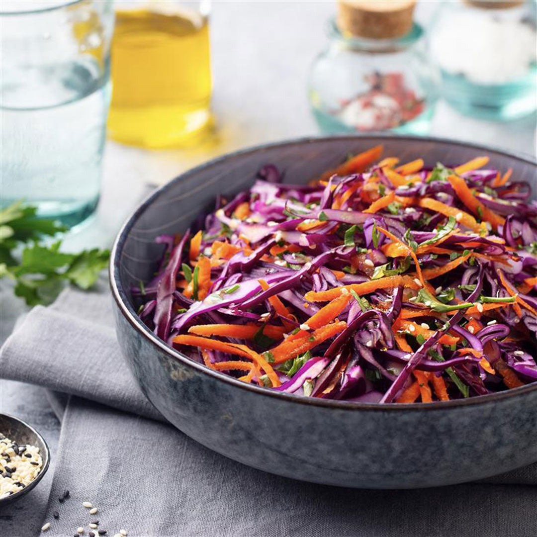 Bowl of shredded purple cabbage and carrots on a gray napkin with a blurred background