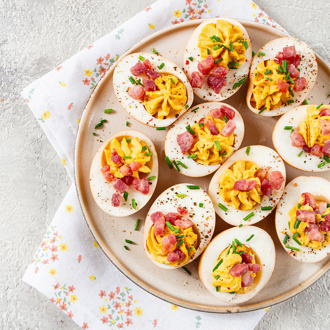 Platter of deviled eggs with ham and chives on a floral cloth.