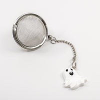 Tea ball with mesh filter and ghost charm on a white background