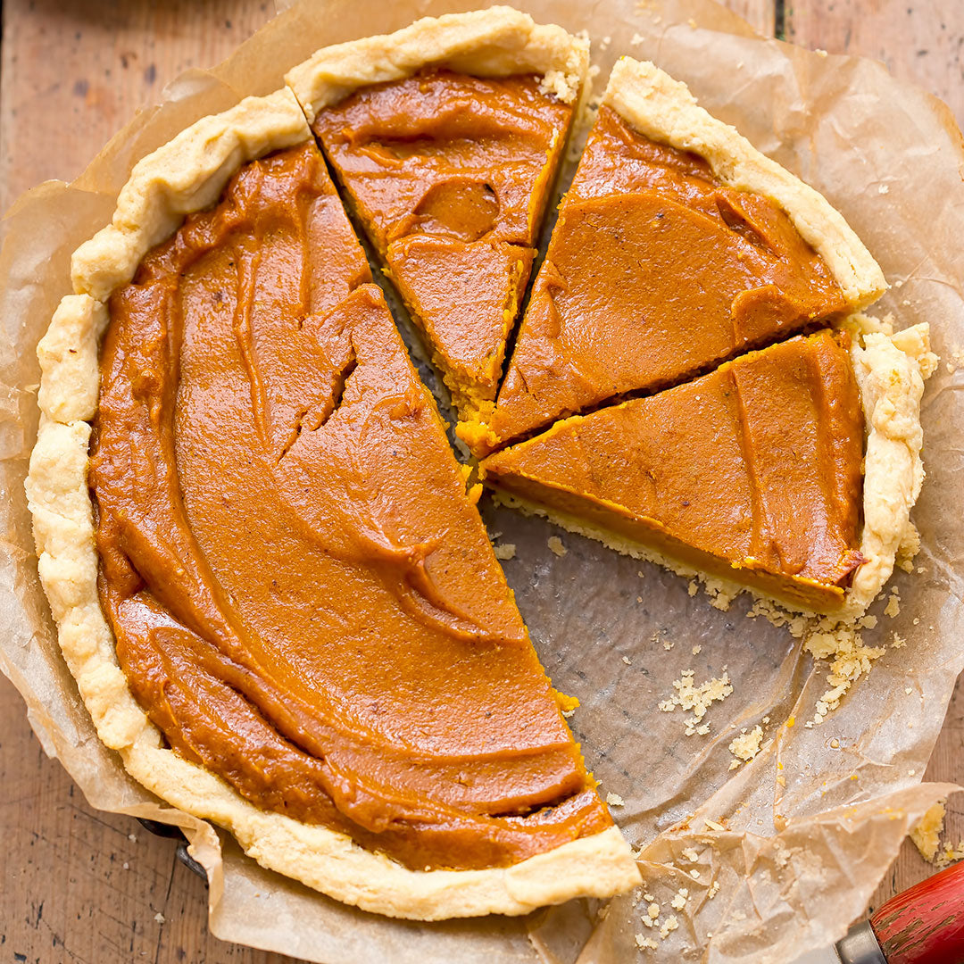 A pumpkin pie with a golden flaky crust, sliced and served on parchment paper over a rustic wooden table.