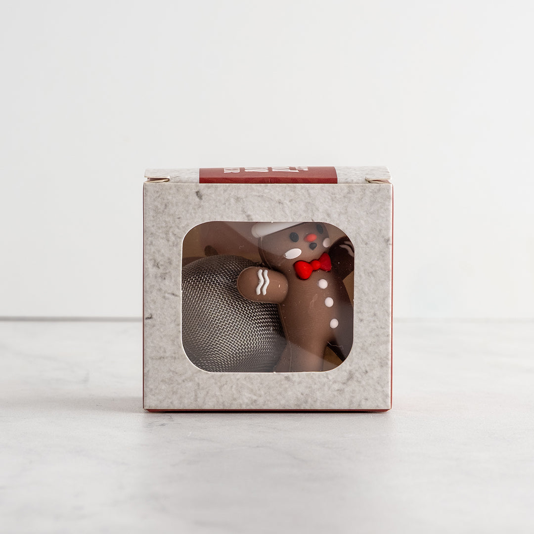 A gingerbread man tea infuser inside a square gray box with a clear front window, set on a light gray surface against a white background.