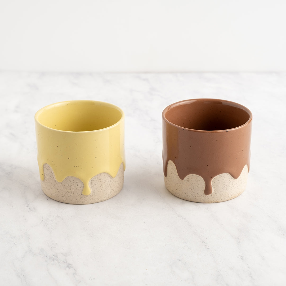 Two ceramic cups, one yellow and one brown, with white accents on a light gray background.