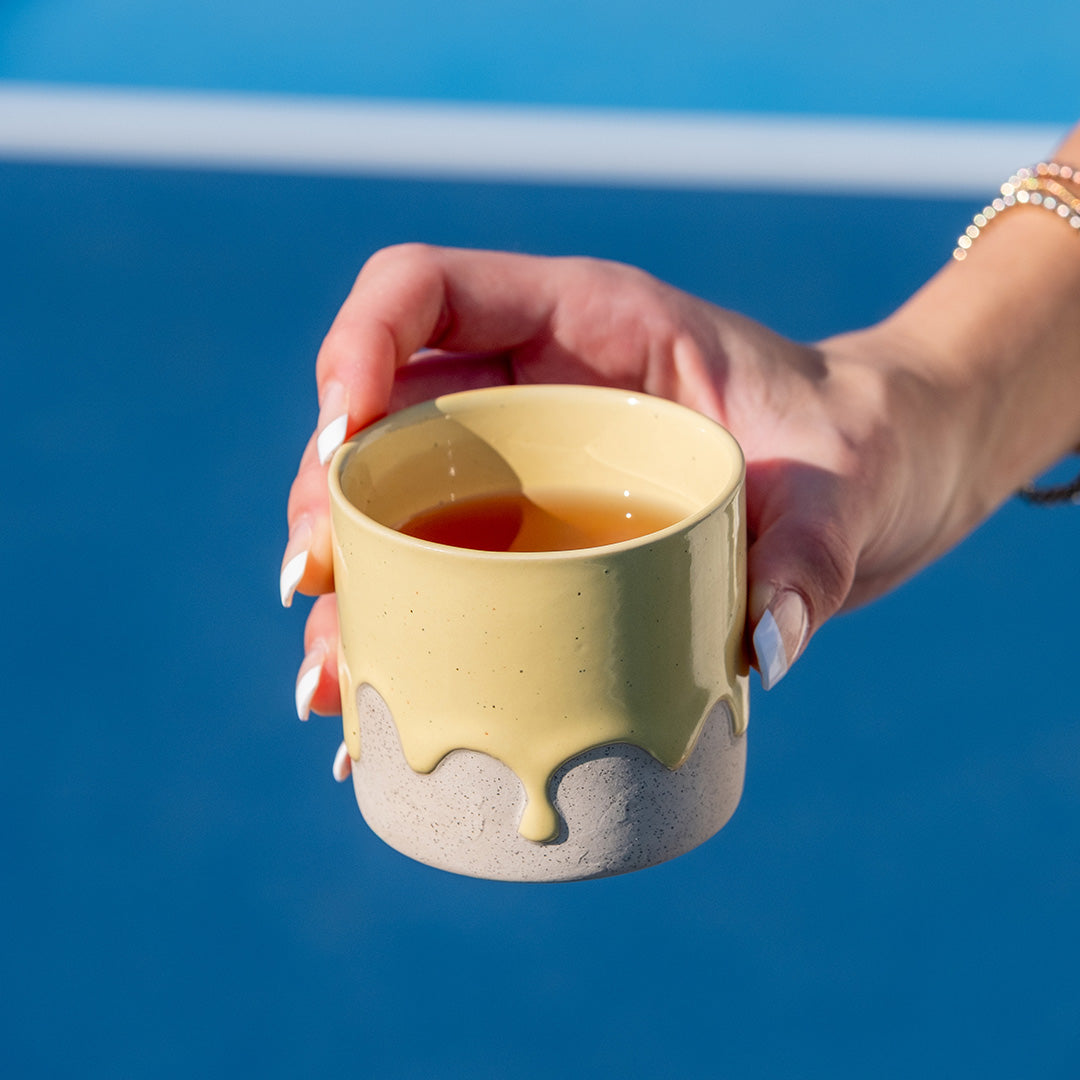 Hand holding a yellow ceramic cup against a blue background