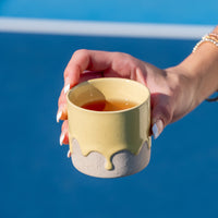Hand holding a yellow ceramic cup against a blue background