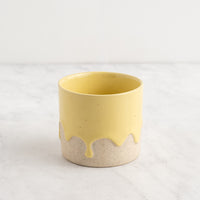 Yellow ceramic cup with beige base on a white background