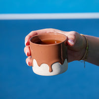 Hand holding a mousee ceramic mug with a white base with a blue background