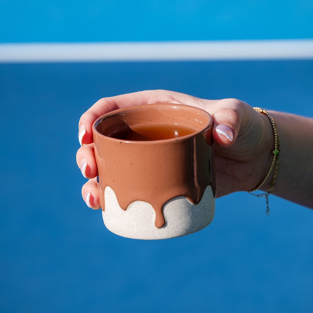Hand holding a mousee ceramic mug with a white base with a blue background