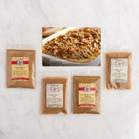 Four bags of seasoning and sugars are arranged on a white marble surface, with a central recipe card showing a prepared sweet potato casserole.