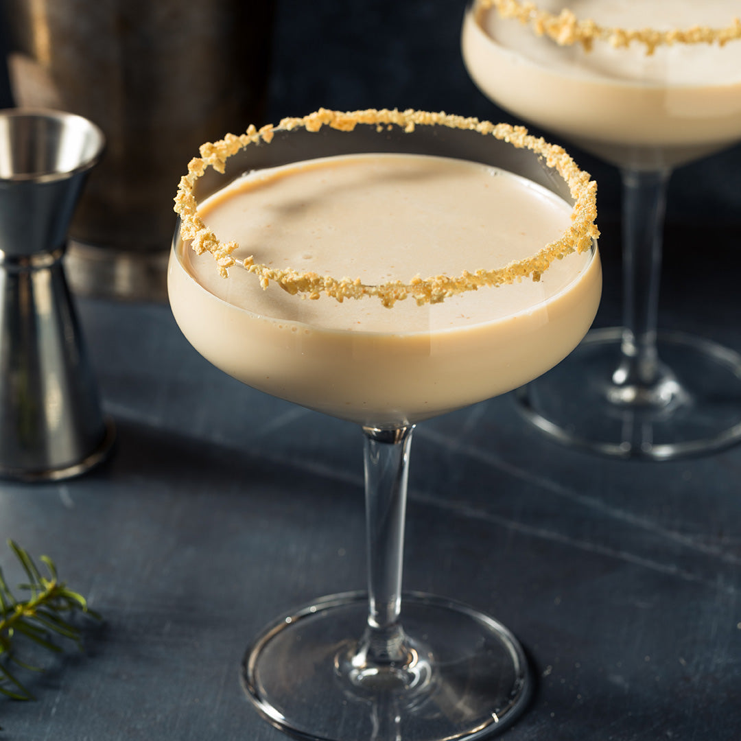 Cocktail with a sugared rim on a dark surface with a jigger and garnish.