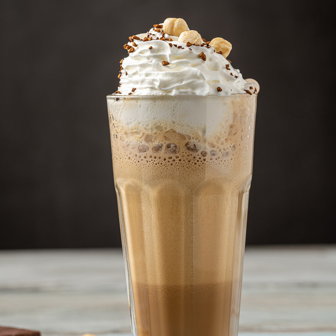 Glass of iced coffee with whipped cream and nuts on a wooden surface